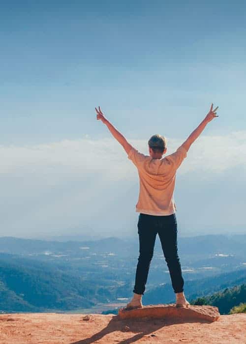 man standing at the top of a mountain holding his arms up