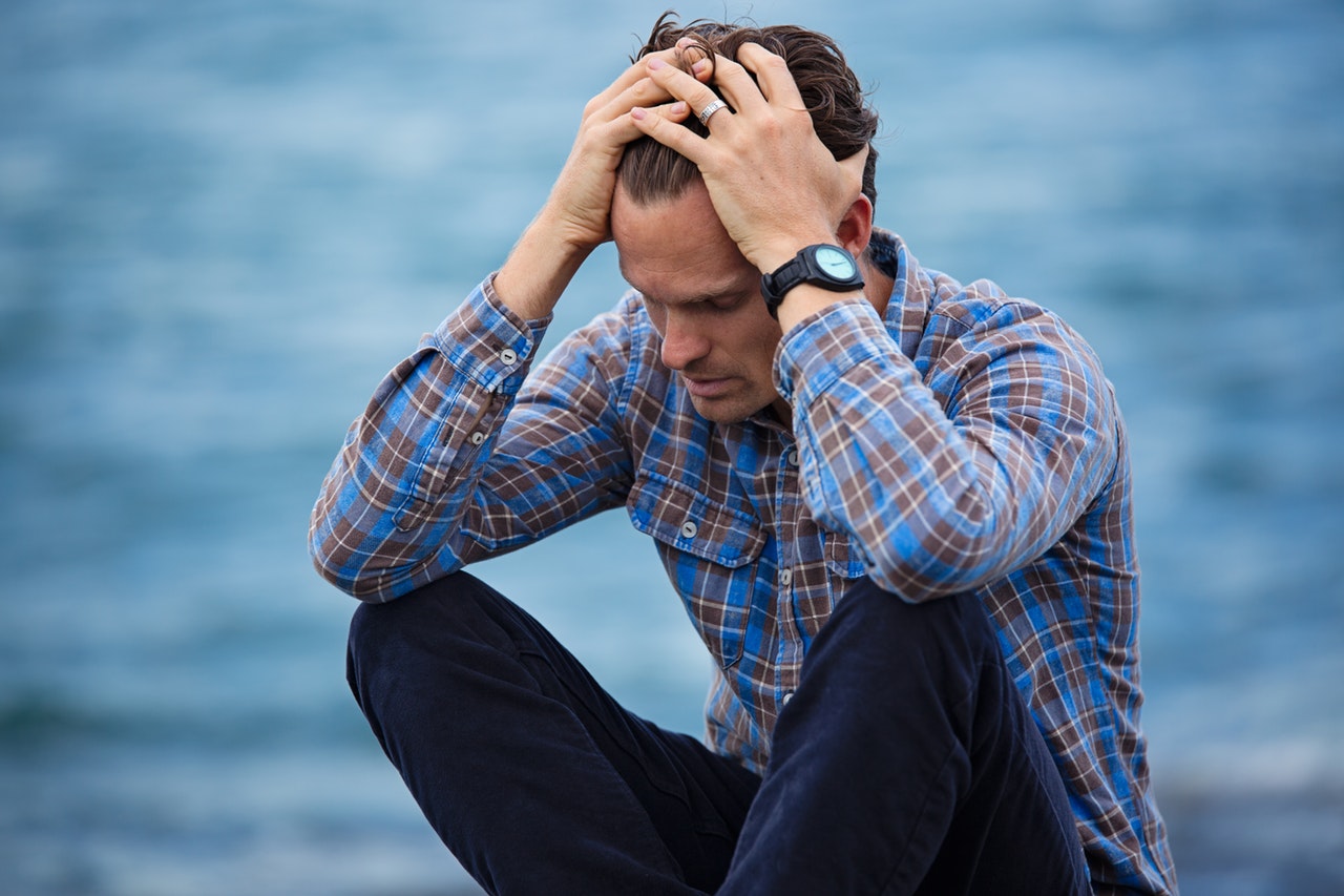 man in blue shirt sitting with his hands on his head worried.