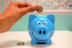 person putting coins into a blue piggy bank
