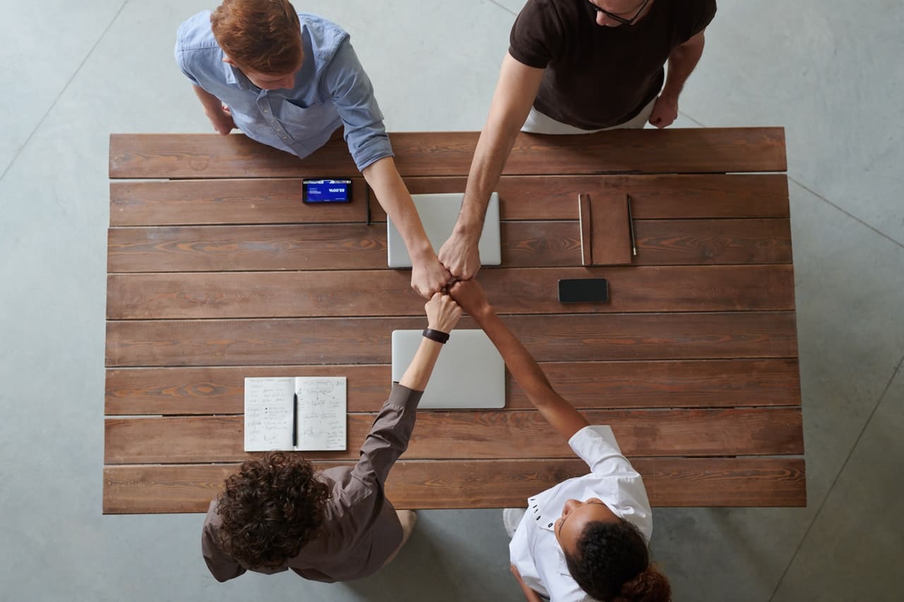 four people at a table doing a fist bump above their work.